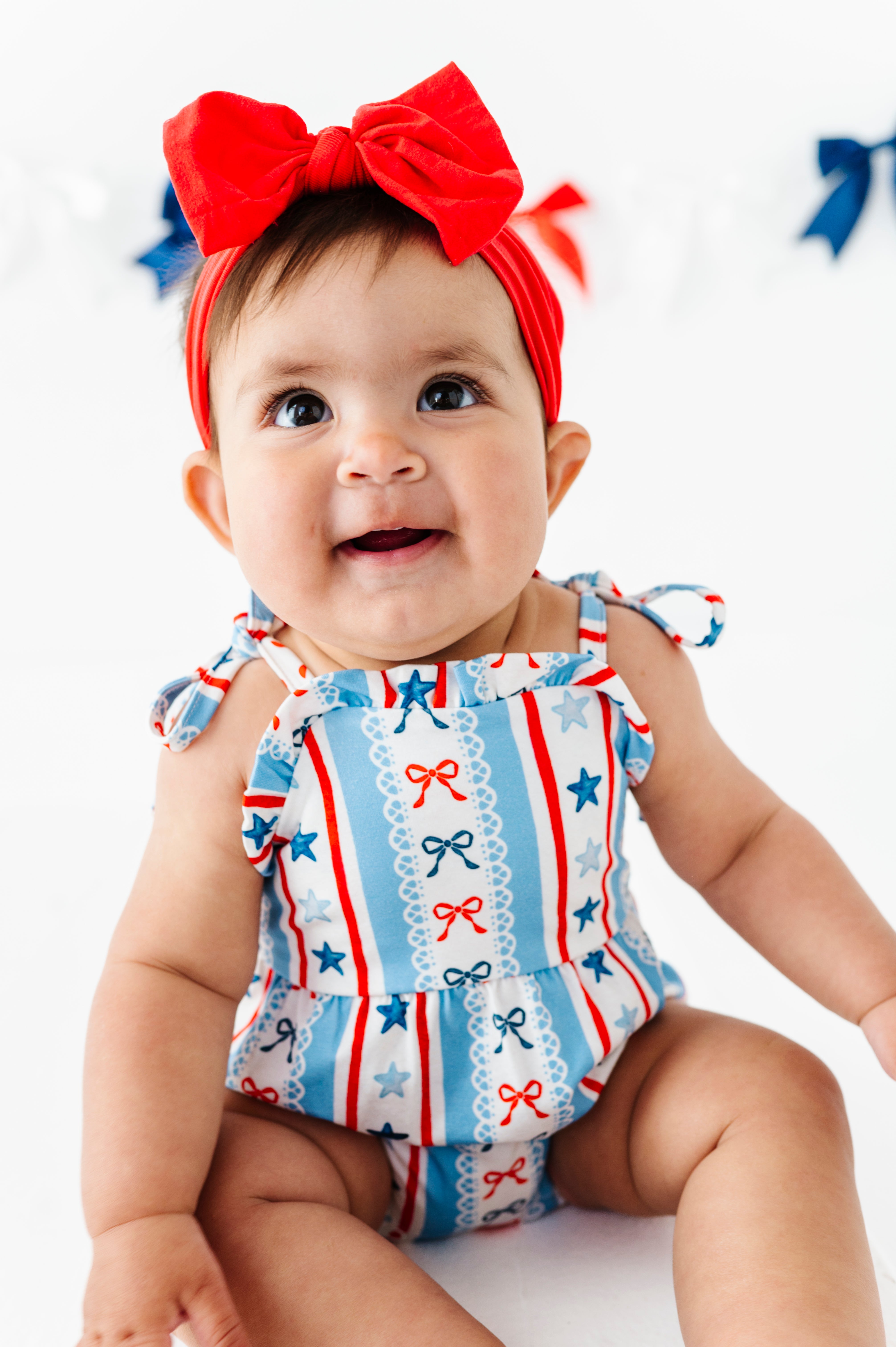Baby wearing a red, white, and blue bamboo bubble romper with a bow on a white background
